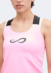 Personne portant un haut sans manches rose clair avec un symbole infini noir sur la poitrine et des bretelles noires et blanches.