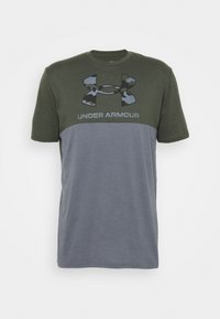 Kortärmad t-shirt i armégrön och grå, med en stor kamouflage Under Armour-logotyp över bröstet. Blandat bomullstyg.
