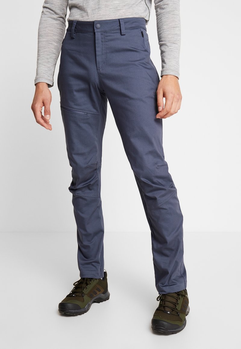 Marineblaue, leichte Hose mit schlanker Passform. Verfügt über einen Knopfverschluss und Reißverschlusstaschen an den Seiten, kombiniert mit dunkelgrünen Wanderschuhen.