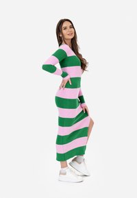 Lungo vestito a righe in verde e rosa. Caratterizzato da un corpetto aderente, maniche lunghe e una spaccatura laterale. Abbinato a sneakers bianche.