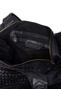 Interno di una borsa in pelle intrecciata nera con una tasca con zip, foderato in tessuto nero. Presenta una cerniera in ottone e un patch con logo impressa sulla pelle.