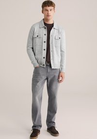 Gråstickad cardigan med två framfickor och mörka knappar, matchad med ljusgrå jeans och bruna mockaskor. Enkel, klassisk design.