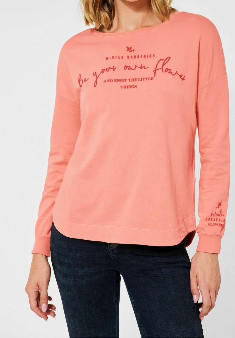 Korallfärgad sweatshirt med långa ärmar som har textgrafik, rund halsringning och en avslappnad passform. Texten inkluderar "Var din egen blomma" och "Vinterträdgård".