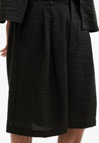 Pantaloni corti neri plissettati realizzati in tessuto testurizzato, con una finitura stropicciata e una vestibilità rilassata, dotati di tasche laterali e cintura.