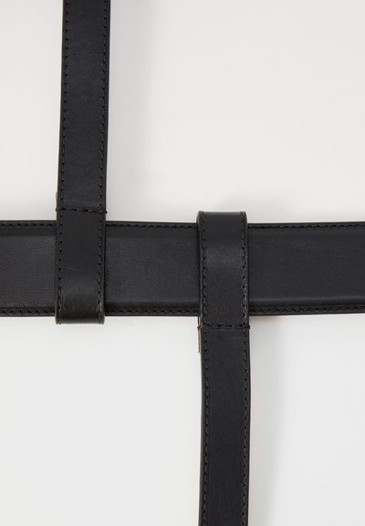 Correas de cuero negro se intersectan a ángulos rectos, con texturas suaves y costuras que contrastan, presentando un diseño limpio y minimalista.