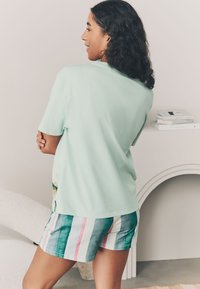 Mētras zaļa kokvilnas T-krekls ar īsām piedurknēm, kombinēts ar svītrainām šortām zaļā, rozā un zilā krāsā. Ikdienišķs, brīvs piegriezums.