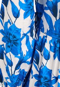 Lilleline kleit, millel on valge taust ja julged sinised lillemustrid, mis demonstreerib erinevaid sinise toone kergetes, tekstuursetes kangastes.