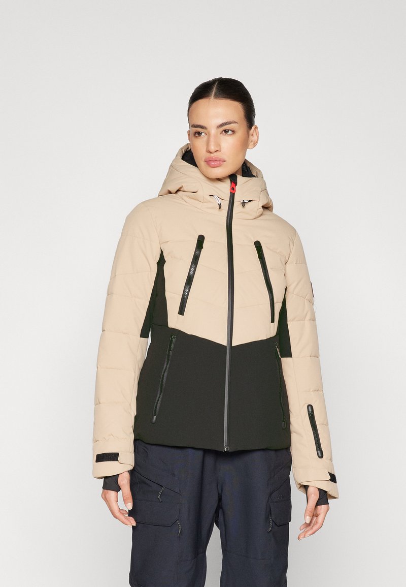 Beige und schwarze isolierte Jacke mit einem Reißverschluss vorne, Kapuze und mehreren Reißverschlusstaschen. Sie hat ein gestepptes Muster an den Ärmeln.