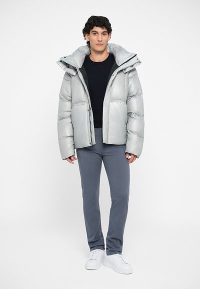 Silver puffer jacket with a high collar, front pockets, and a shiny texture, worn over a dark top and gray pants, paired with white sneakers.