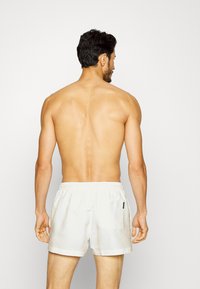 Costumi da bagno bianchi con vita elasticizzata, tasche laterali e una tasca posteriore, realizzati in un tessuto leggero e morbido.