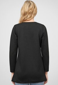 Zwarte lange mouwen tuniek met een geribbelde textuur, voorzien van een ronde halslijn en een licht uitlopende zoom. Ontworpen voor comfort met een ontspannen pasvorm.