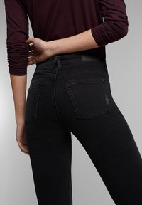 Jeans de mezclilla negra con un diseño ajustado, que cuentan con dos bolsillos traseros y una cinturilla con un lazo. El material parece suave con un ligero estiramiento.