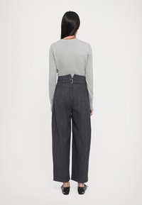 Pull en tricot gris avec une fente en V au dos, associé à un pantalon taille haute gris foncé à rayures avec un détail de boucle.