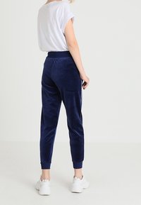 Námořnické modré sametové joggers s tapered designem, elastickým pasem a manžetami, spárované s volným bílým tričkem s kulatým výstřihem a bílými teniskami.