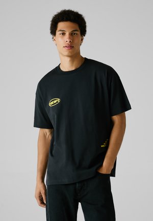Zwarte katoenen t-shirt met een ontspannen pasvorm, voorzien van gele graphics op de borst en zoom. Zachte textuur en korte mouwen.