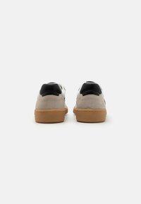 Zamszowe i skórzane tenisówki z czarnym obcasem, białą cholewką i gumową podeszwą. Cechują się teksturowanym wzorem i przeszyciami wzdłuż krawędzi.