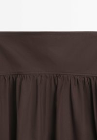 Jupe en tissu marron avec un design froncé à l'ourlet. Texture lisse et ceinture élastique, offrant une silhouette fluide.