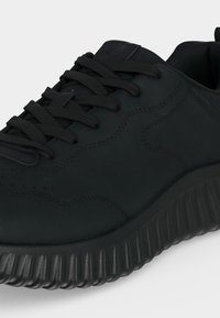 Baskets de sport noires avec semelle texturée, fermeture à lacets et logo embossé sur la languette, vues de côté et de dessus.