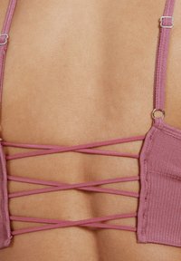 Lace-back bralette in gedempt roze stof; heeft dunne bandjes en een kruisontwerp op de rug, met een zachte textuur.
