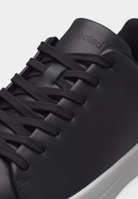 Μαύρο δερμάτινο αθλητικό παπούτσι με μαύρα κορδόνια, λείο φινίρισμα και ανάγλυφο όνομα μάρκας στη γλώσσα, σε συνδυασμό με λευκή ελαστική σόλα.