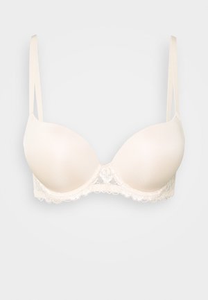 Beżowy biustonosz bez szwów z koronkowym wykończeniem, z regulowanymi ramiączkami i gładką teksturą. Okrągłe miseczki i ozdobna koronka przy obwodzie.