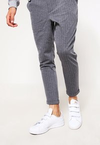 Pantalones grises a rayas con un corte entallado y bajos con puño, combinados con zapatillas blancas con tiras de Velcro.