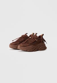 Brune teksturerede sneakers med en klodset sål, der har vævet mesh materiale, fremtrædende runde snørebånd og en sløjfepull-tab ved hælen.