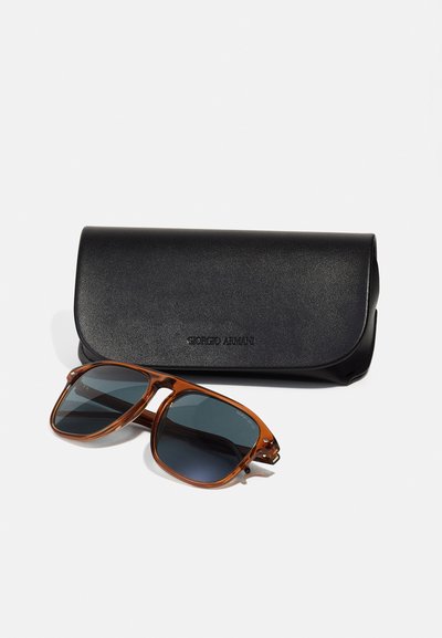 Lunettes de soleil en acétate marron avec des verres sombres, accompagnées d'un étui en cuir noir embossé avec "Giorgio Armani." Les lunettes présentent un design de monture angulaire.