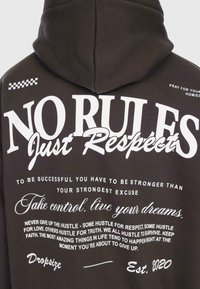 Sudadera de color marrón oscuro con un gran texto gráfico blanco en la parte posterior. Presenta frases motivacionales en diversas tipografías, capucha y una textura suave.