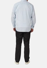 Hellblaues Langarmhemd mit Rückenteil, Knopfmanschetten und schwarzer Hose. Das Hemd hat eine dezente Struktur und sitzt locker.