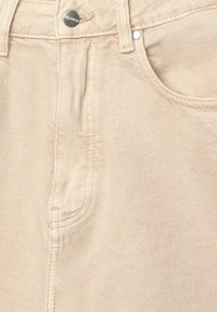 Beige Jeans mit klassischem Fünf-Taschen-Design, Metallknopfverschluss und sichtbaren Nähten im gesamten Bereich.