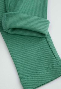 Zielony materiał żebrowany z zagiętym mankietem i widocznym przeszyciem, ukazujący teksturę i wzór dzianiny na płaskiej jasnej powierzchni.