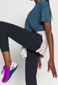 Tyrkis kortærmet t-shirt, sorte leggings og lyserøde/hvide løbesko med blå sål. Lagdelt lyserød skjorte bundet i taljen.