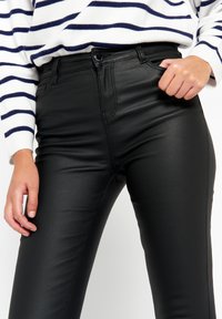 Čierne skinny džínsy z umelej kože s hladkou textúrou a vysokým pásom. Majú predné vrecká a detailné šitie.