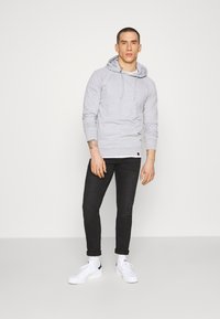 Szürke kapucnis pulóver kenguru zsebbel és húzózsinórral. Fekete, slim-fit farmernadrággal és fehér sportcipővel párosítva. Egyszerű, laza megjelenés.