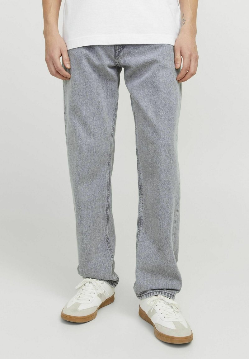 Jeans rectos de color gris claro con costuras visibles, textura ligeramente desgastada y un corte relajado; combinados con zapatillas deportivas blancas.