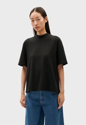 Black short-sleeve t-shirt with a mock neckline, made of soft fabric. Paired with blue wide-leg pants, featuring a relaxed fit.