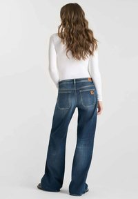 Jeans de mezclilla azul marino con un diseño de pierna ancha, que presentan una cintura alta, dos bolsillos traseros y un parche de cuero con la marca en la cinturilla.