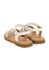 Sandalias de cuero blancas con detalles de tira trenzada, hebilla ajustable en el tobillo y suela marrón texturizada. Diseñadas para comodidad y estabilidad.