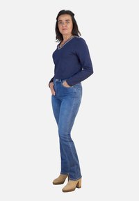 Top de manga larga en navy con escote en V, combinado con jeans ajustados de un azul claro y zapatos de plataforma beige, destacando un estilo simple y casual.