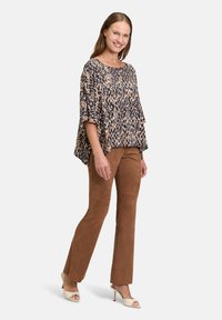 Ponczosz z nadrukiem zwierzęcym z krótkimi rękawami w odcieniach beżu i granatu, połączony z brązowymi spodniami z zamszu i kremowymi sandałami na obcasie.