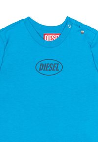 T-shirt turchese in cotone con collo rotondo, maniche corte e logo ovale nero "DIESEL" sul davanti. Dettaglio a clip sulla spalla.