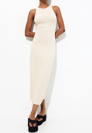 Beige, nauwsluitende tankjurk met een slanke silhouet, tot op de knie. Gecombineerd met zwarte platformsandalen met een strikaccent.