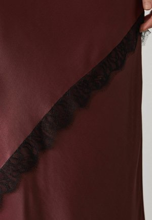 Dark burgundy satin fabric with diagonal black lace trim held by a hand on the upper right side.