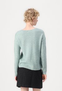 Suéter de malha azul-petróleo com um ajuste descontraído, mangas longas, textura canelada e decote baixo nas costas. Combinado com uma saia texturizada escura.