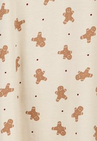 Roomkleurige stof met een herhalend patroon van bruine peperkoekfiguren en bordeauxrode stippen, met een gladde textuur en een speels ontwerp.