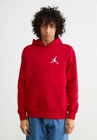Rød hættetrøje lavet af blødt stof med en kengurulomme, prydet med et hvidt Jumpman-logo på brystet samt ribbede manchetter og kant.