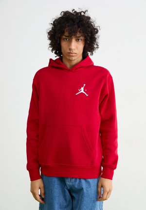 Rød hættetrøje lavet af blødt stof med en kengurulomme, prydet med et hvidt Jumpman-logo på brystet samt ribbede manchetter og kant.