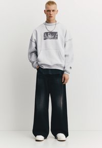 Grå oversized sweatshirt med grafisk tryk på fronten, stylet med vide mørk denim jeans og hvide sneakers. Sølvkæde som accessory.