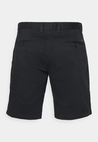 Pantaloni corti neri realizzati in un tessuto dalla superficie liscia. Presentano due tasche posteriori con bottoni e dettagli cuciti lungo la vita.